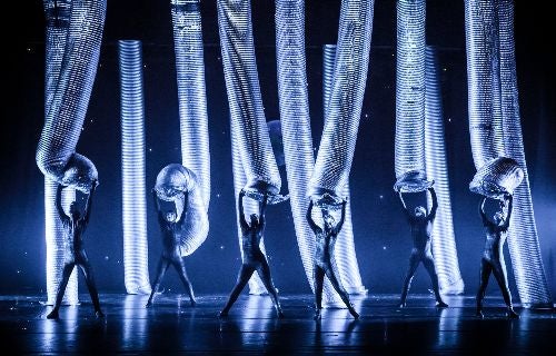 Stage performance with dancers holding large illuminated flexible tubes, creating a futuristic visual display.