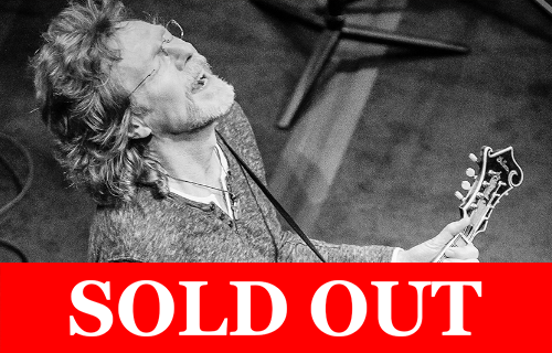 Black-and-white image of a musician playing guitar with eyes closed, overlaid with ‘SOLD OUT’ in bold red text.